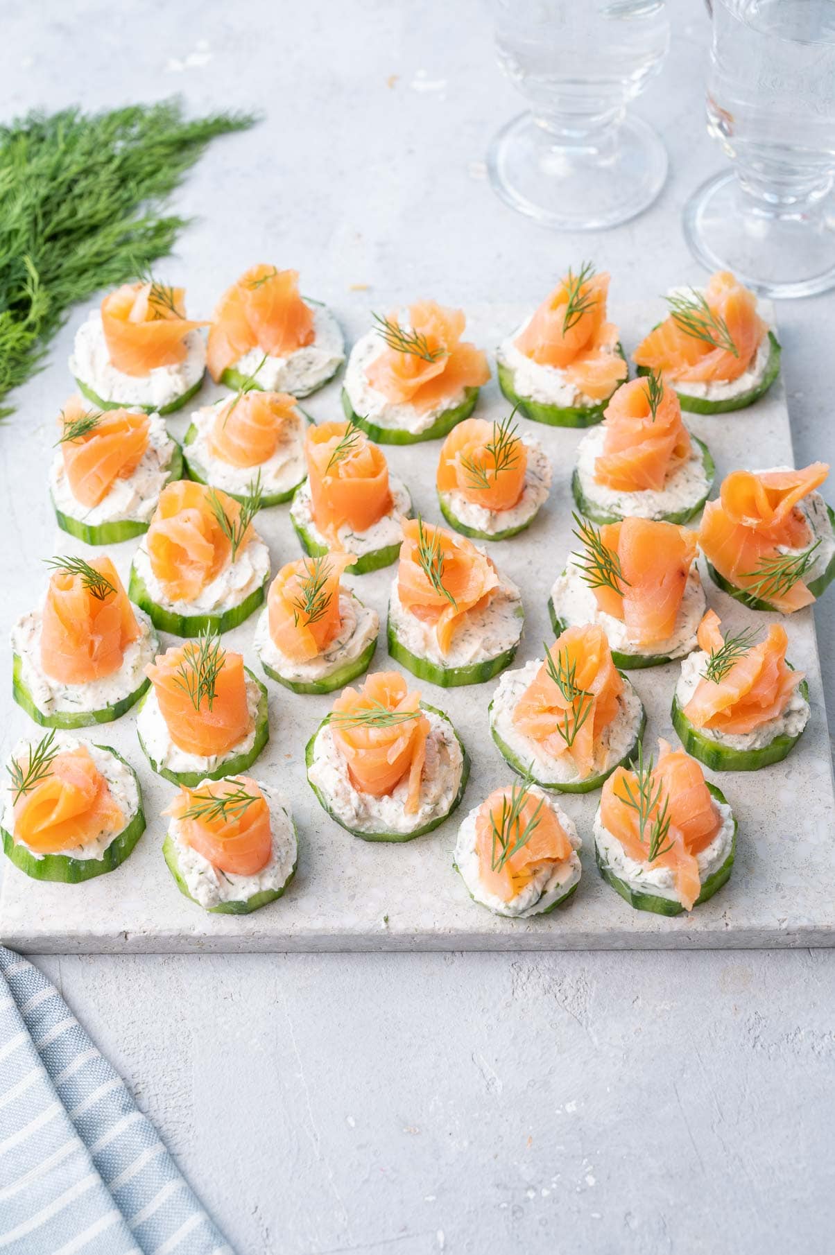 Smoked salmon cream cheese cucumber bites on a white stone board.