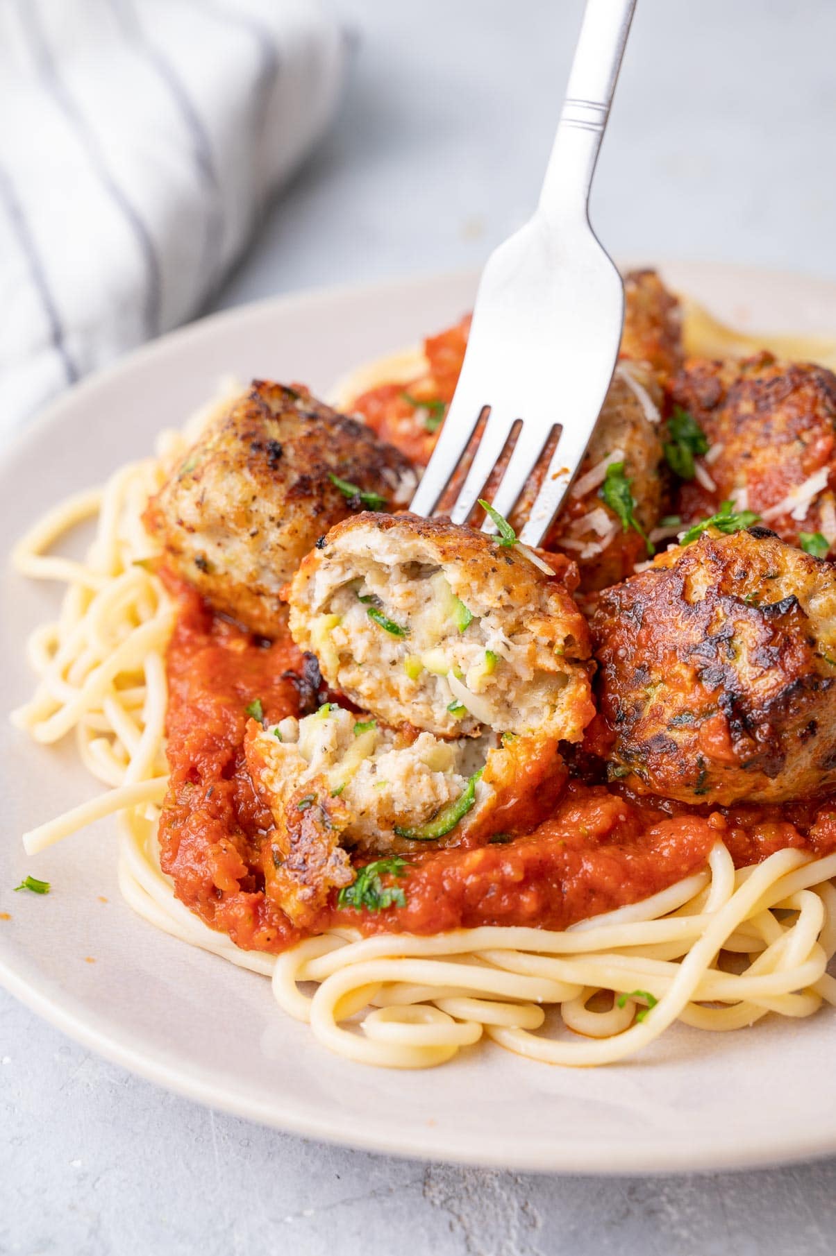 Cut in half meatball stuck on a fork. Turkey meatballs with tomato sauce and spaghetti on a beige plate.