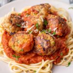 Turkey zucchini meatballs with tomato sauce and spaghetti on a beige plate.