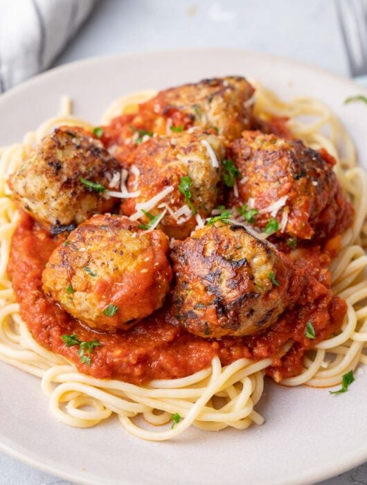 Turkey zucchini meatballs with tomato sauce and spaghetti on a beige plate.