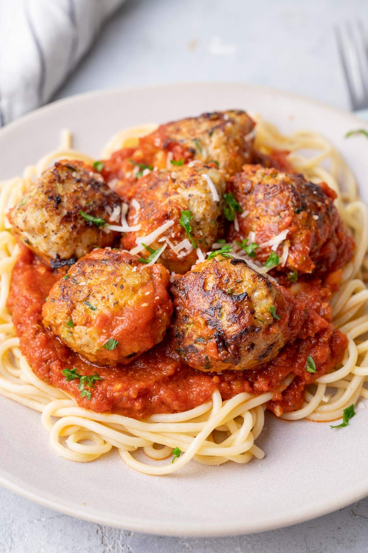 Turkey zucchini meatballs with tomato sauce and spaghetti on a beige plate.