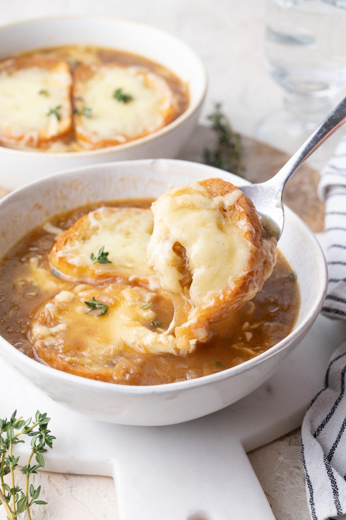 A piece of cheesy baguette is being picked up with a spoon from the French onion soup.