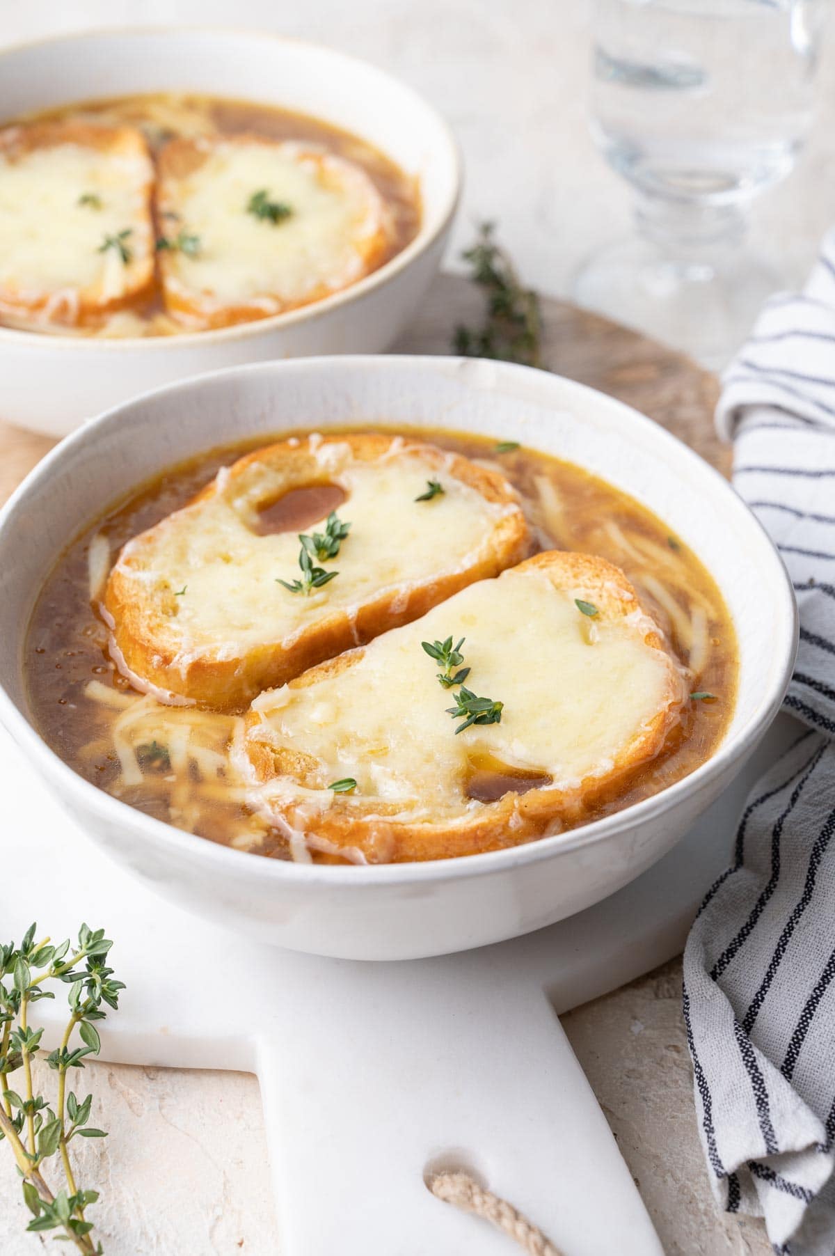 French onion soup in a white bowl topped with two pieces of cheesy baguette.