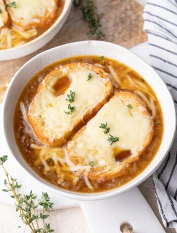 French onion soup topped with cheesy bread in a white bowl.