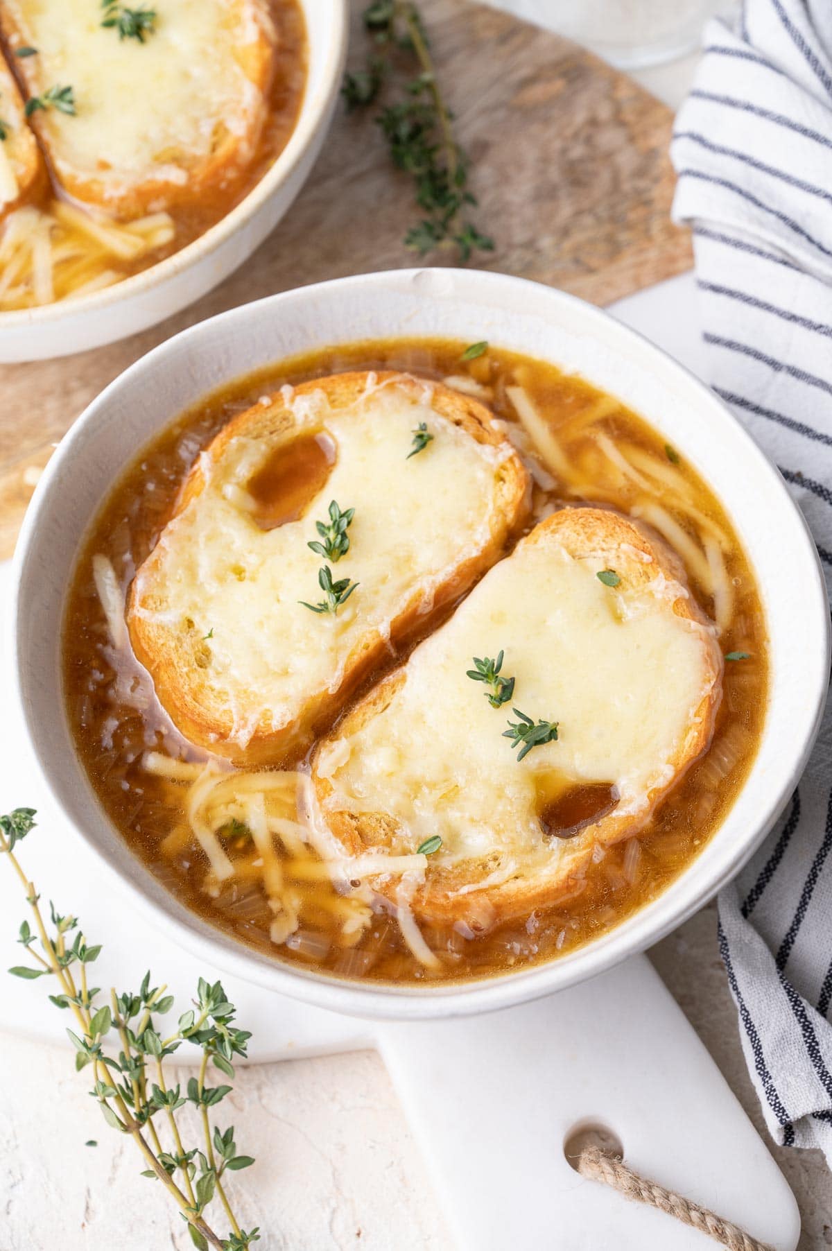 French onion soup in a white bowl topped with two pieces of cheesy baguette.