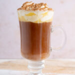 A glass with amaretto coffee topped with whipped cream and cinnamon.