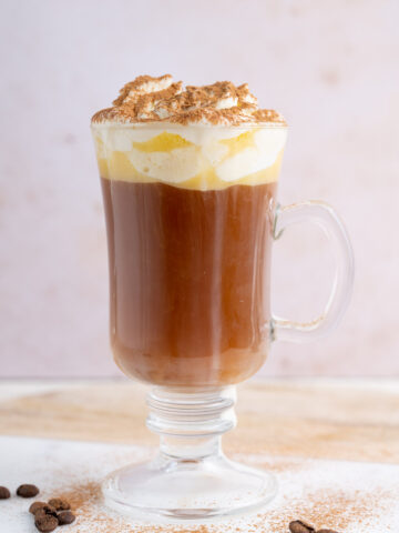 A glass with amaretto coffee topped with whipped cream and cinnamon.
