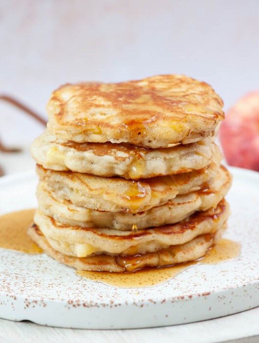 A stack of apple cinnamon pancakes on a white plate.