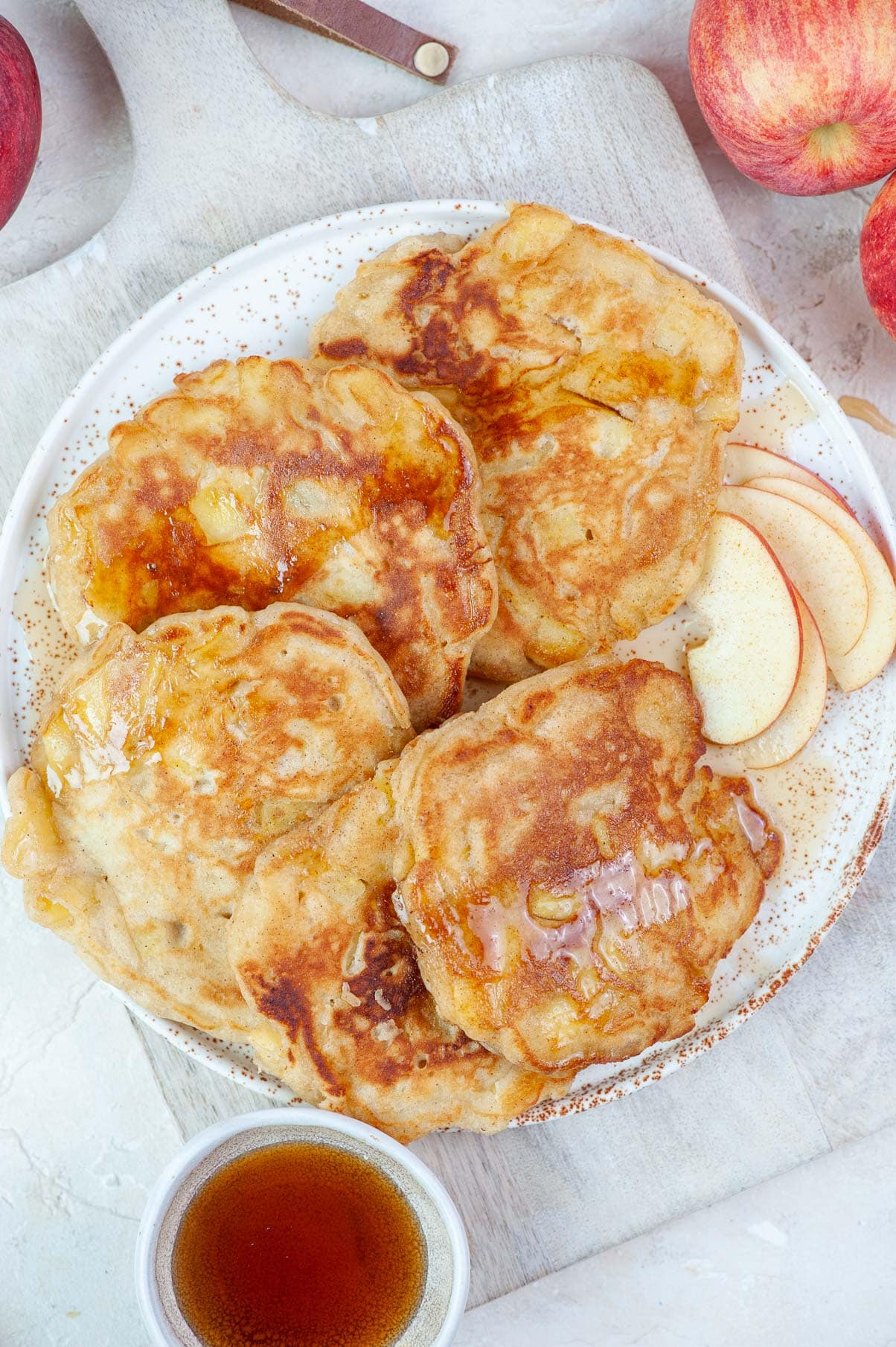 Apple cinnamon pancakes on a white table drizzled with maple syrup.