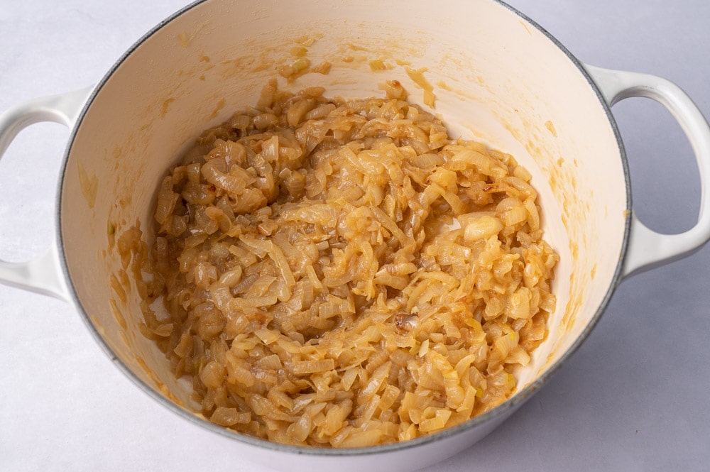 Partially caramelized onions in a white pot.