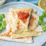 Cheese quesadillas on a green plate topped with tomato salsa.