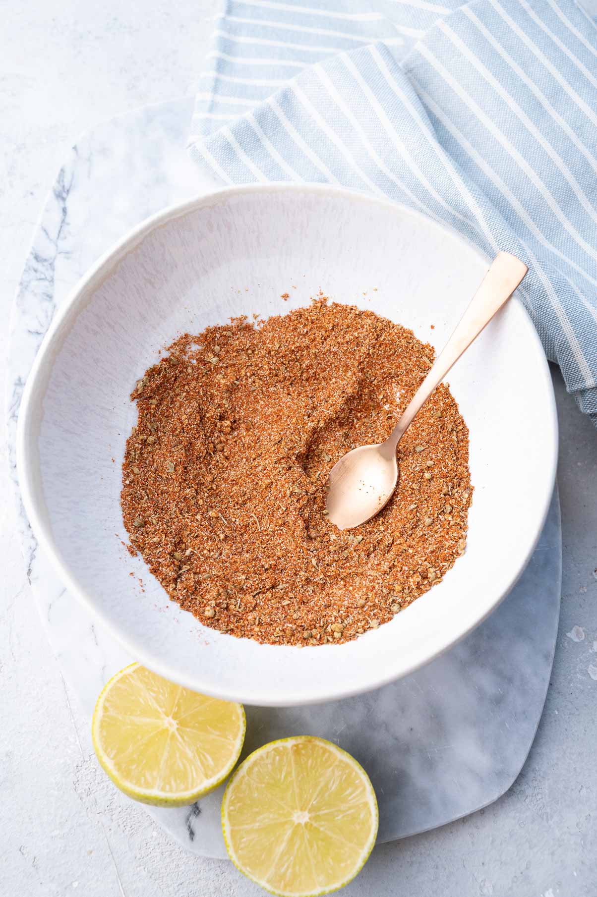 Fajita seasoning in a white bowl. Limes and kitchen cloth on the side.