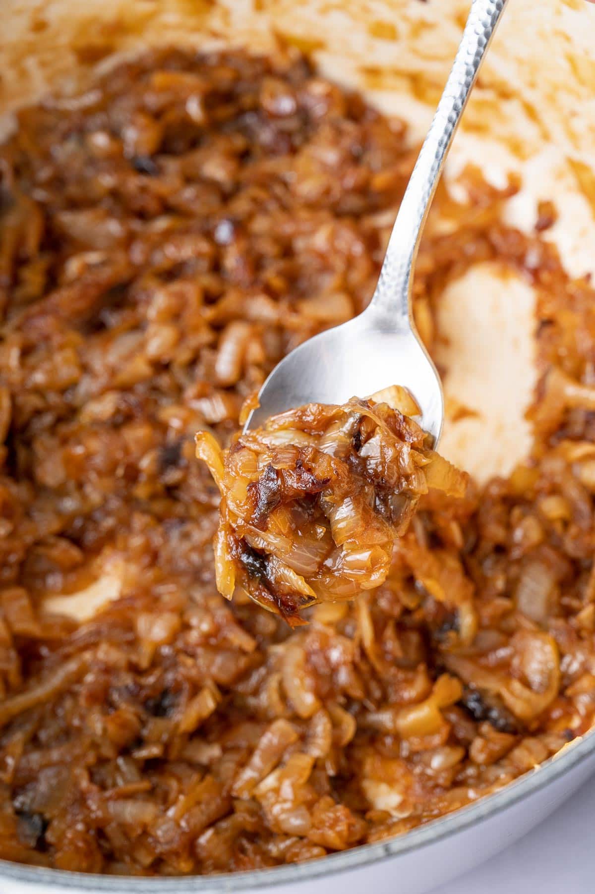 Caramelized onions on a spoon. Pot with onions in the background.