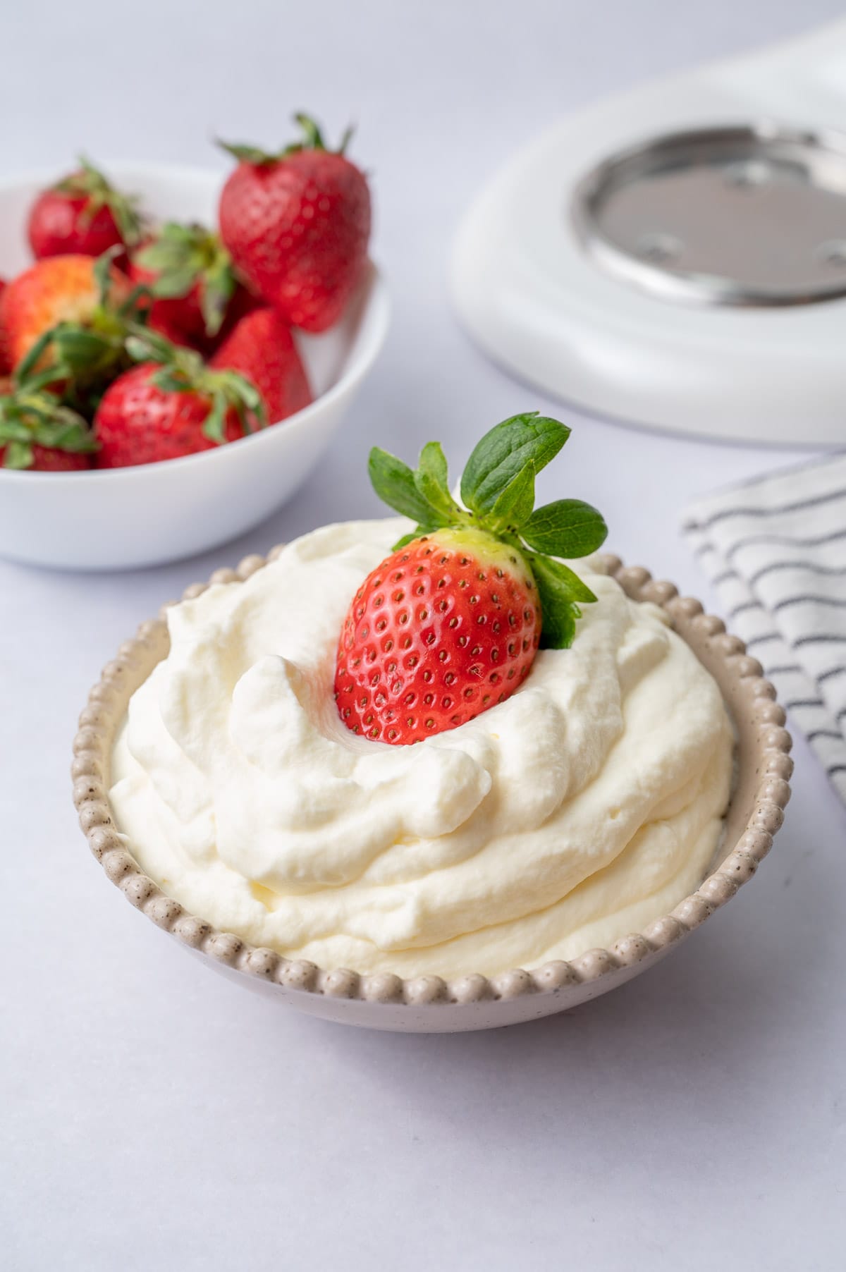 Whipped cream in a beige bowl with a strawberry on top.