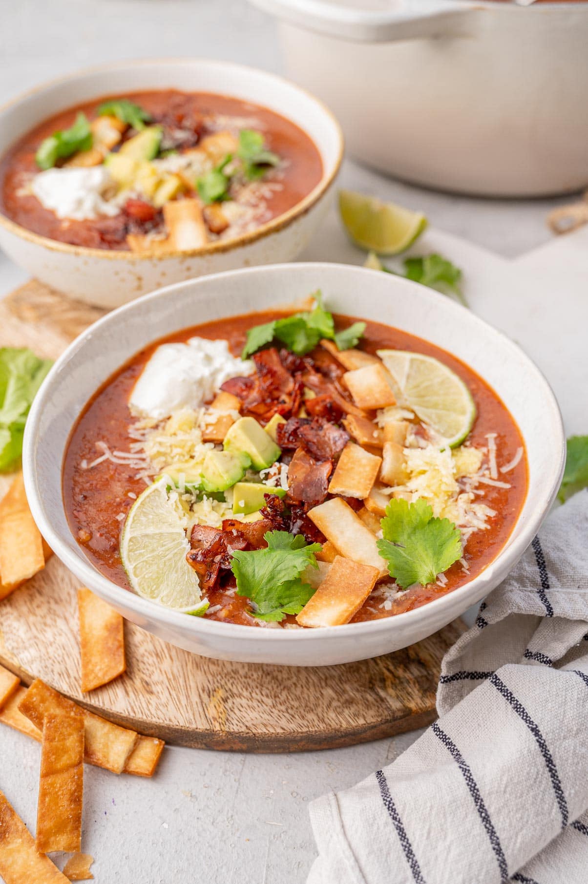 Kidney bean soup topped with avocado, bacon, tortilla strips, and cheese in a white bowl.