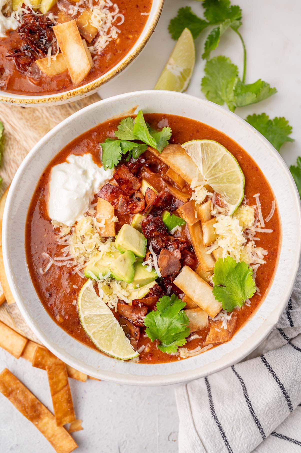 Kidney bean soup topped with avocado, bacon, tortilla strips, and cheese in a white bowl.