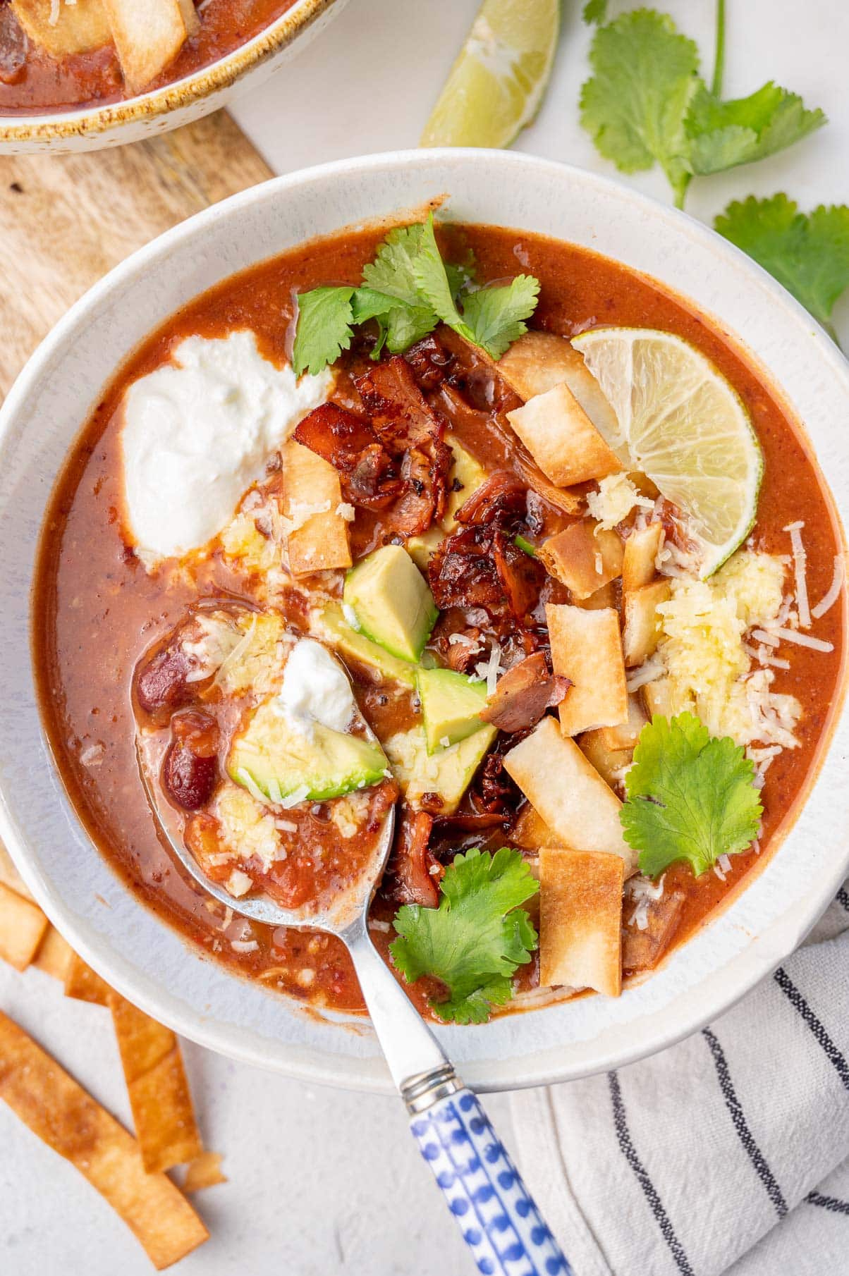 Kidney bean soup topped with avocado, bacon, tortilla strips, and cheese in a white bowl.
