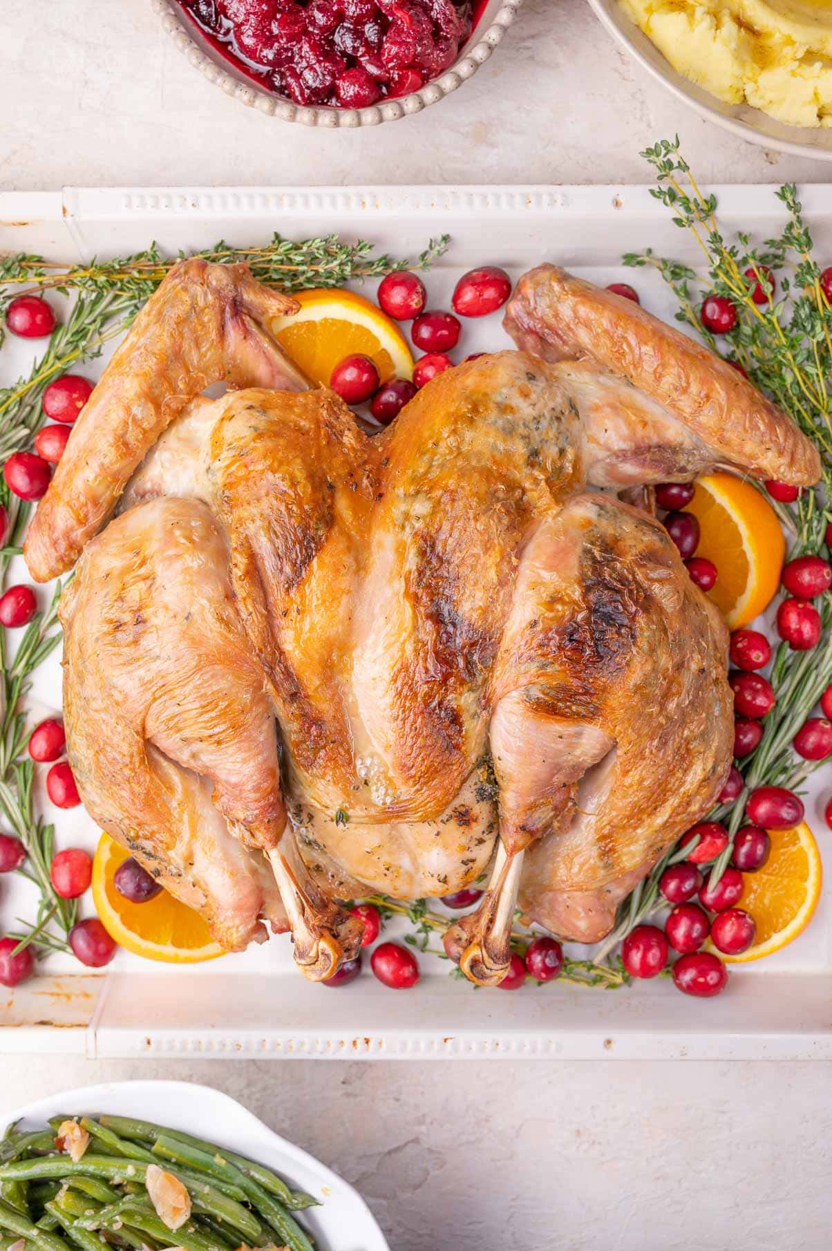 Spatchcock turkey on a baking sheet surrounded with oranges, cranberries, and herbs.