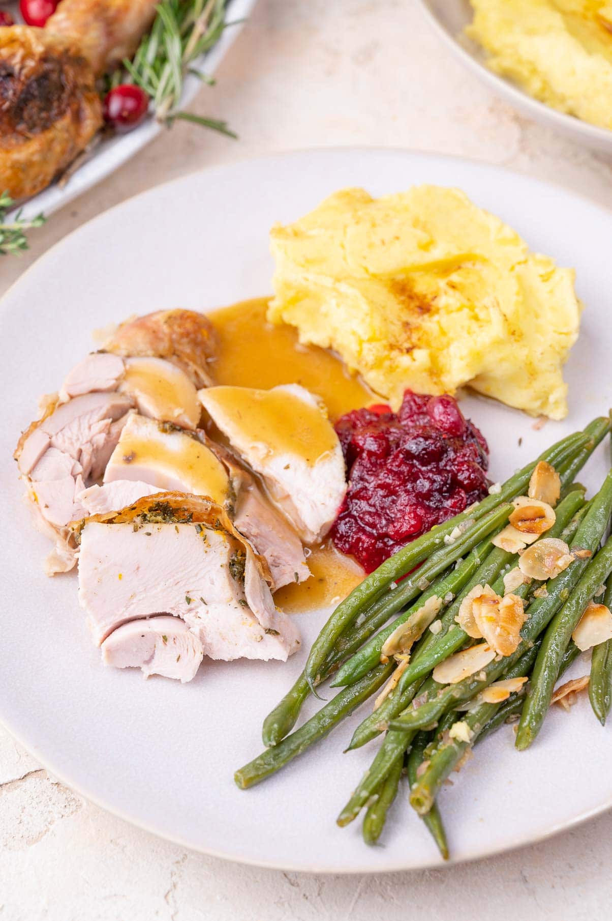 Roast turkey, mashed potatoes, gravy, cranberry sauce, and green beans on a beige plate.