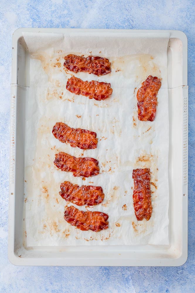 Cooked bacon slices on a baking sheet lined with parchment paper.