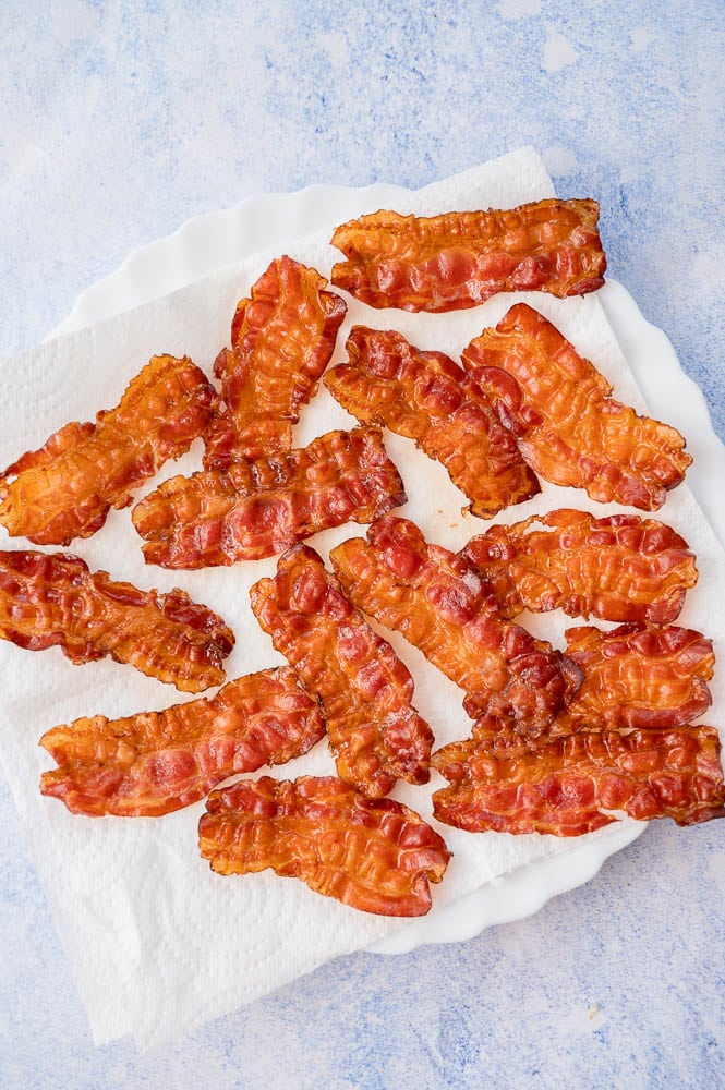 Baked bacon slices on a white plate lined with paper towels.