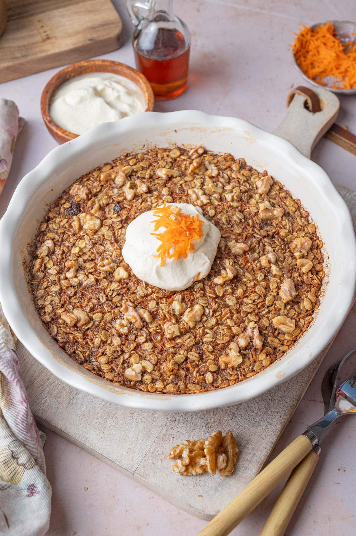 Baked carrot cake oatmeal in a white baking dish topped with cream cheese topping and grated carrots.