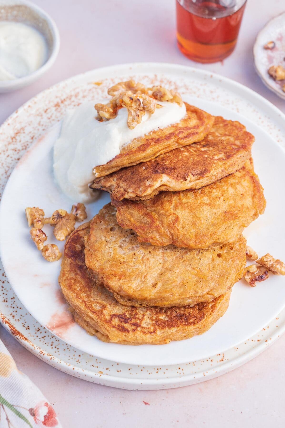 Carrot cake pancakes topped with cream cheese frosting on a white plate.
