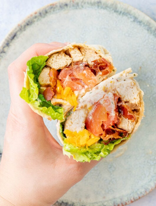 Two halves of chicken bacon ranch wrap are being held in a hand.