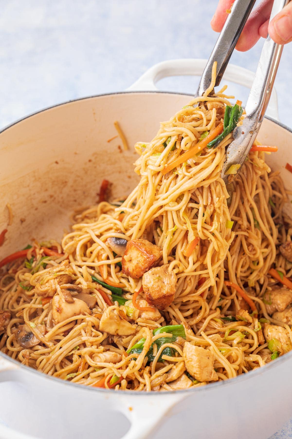 Noodles are being picked from a pot with kitchen tongs.