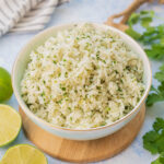 Cilantro lime rice in a blue bowl surrounded with cilantro and limes.