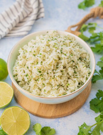 Cilantro lime rice in a blue bowl surrounded with cilantro and limes.