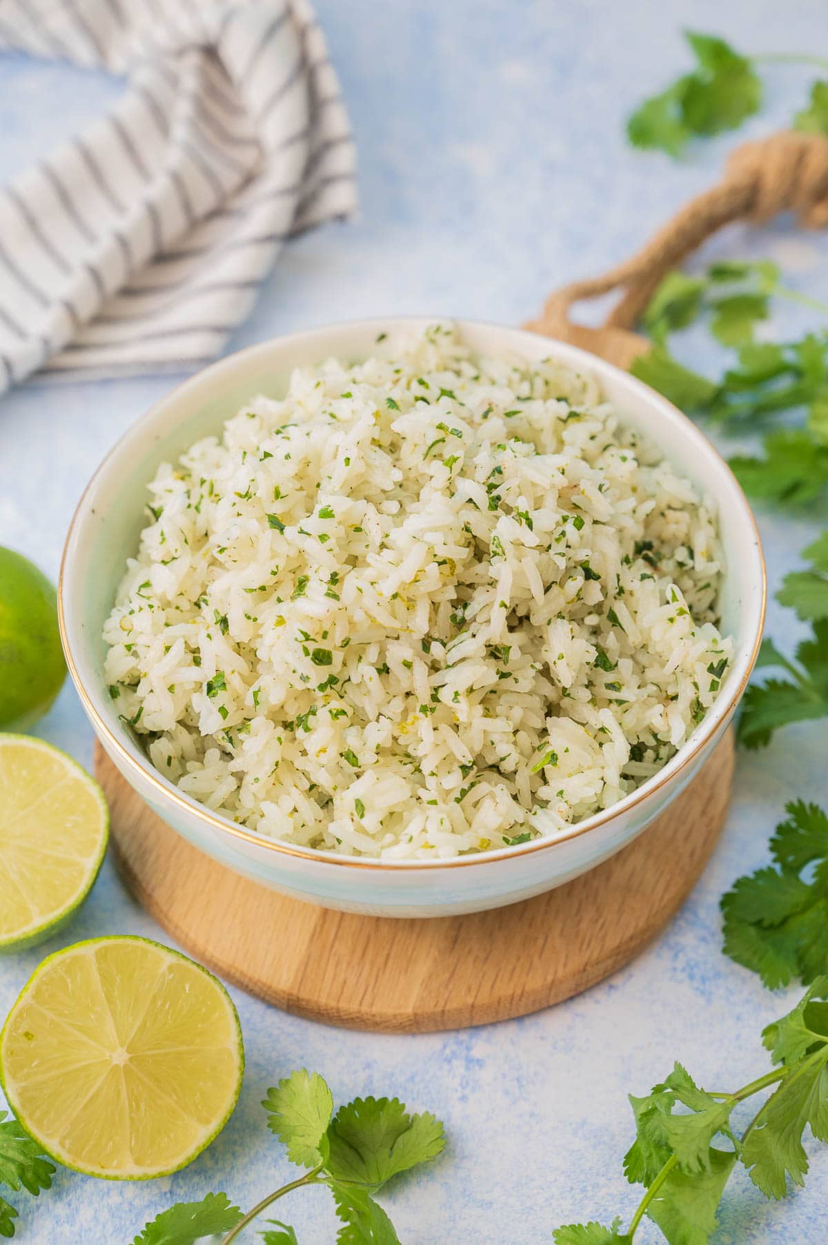 Cilantro lime rice in a blue bowl surrounded with cilantro and limes.