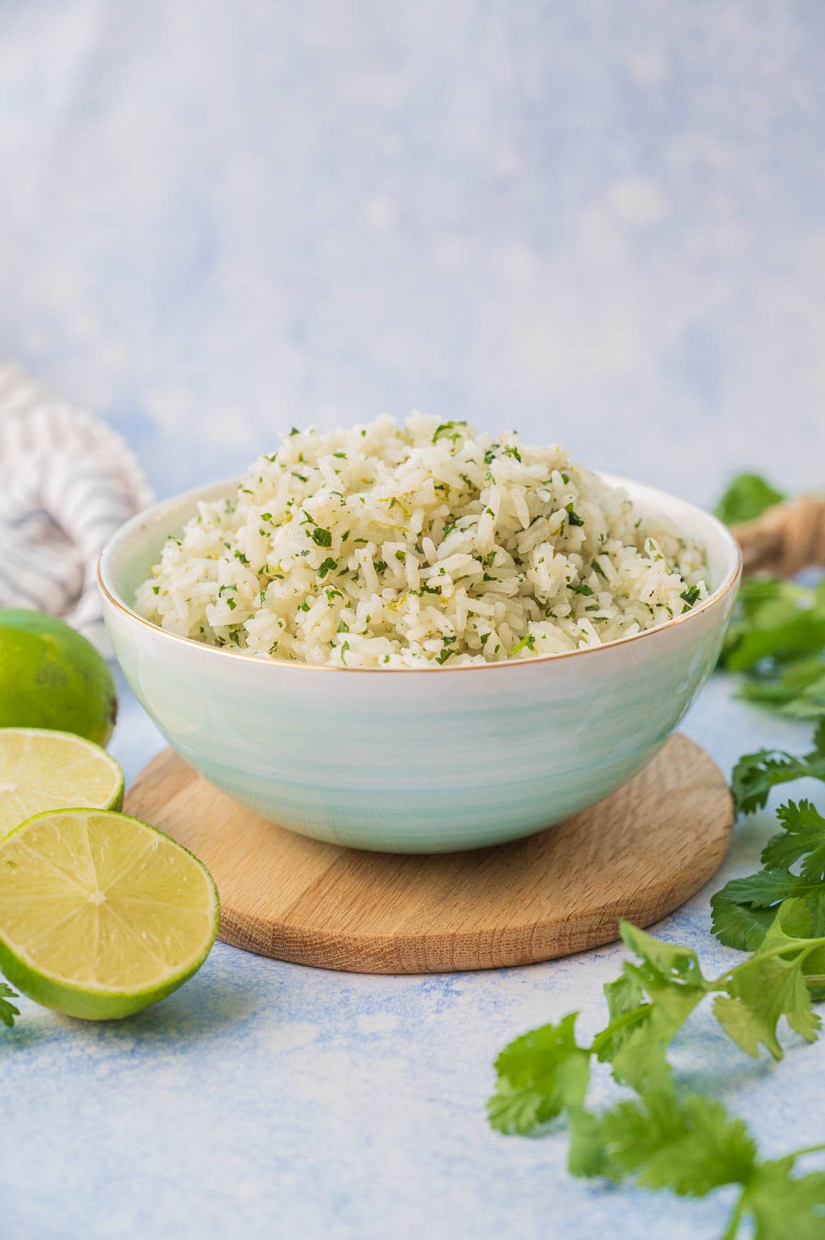 Cilantro lime rice in a blue bowl surrounded with cilantro and limes.