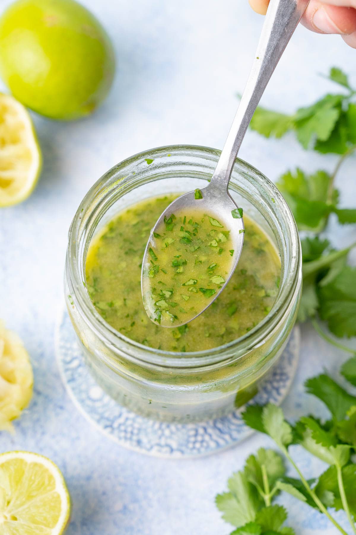 Cilantro lime vinaigrette in a jar and on a spoon. Cilantro and limes in the background.