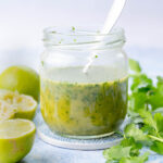 Cilantro lime vinaigrette in a jar. Cilantro and limes in the background.