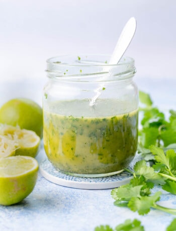Cilantro lime vinaigrette in a jar. Cilantro and limes in the background.