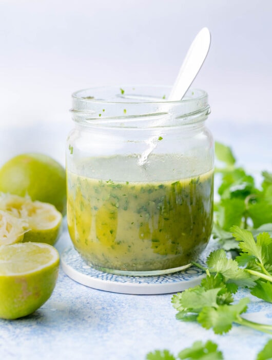 Cilantro lime vinaigrette in a jar. Cilantro and limes in the background.