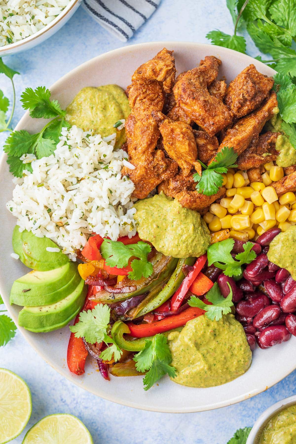 Chicken fajitas with corn, avocado, beans, cilantro lime rice, and sauce in a beige bowl.