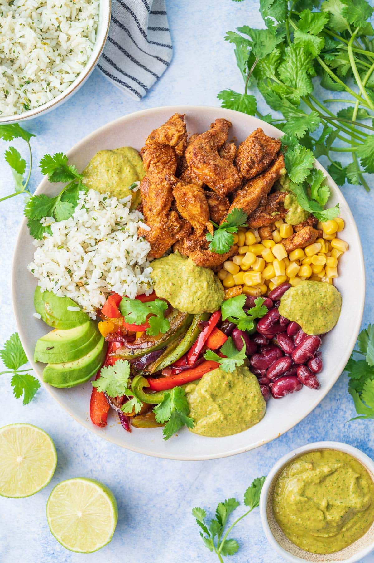 Chicken fajitas with corn, avocado, beans, cilantro lime rice, and sauce in a beige bowl.