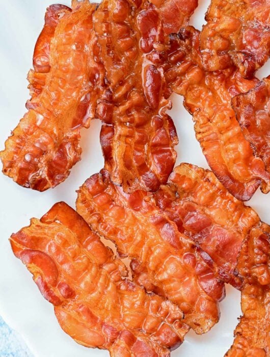 Baked bacon slices on a white plate.