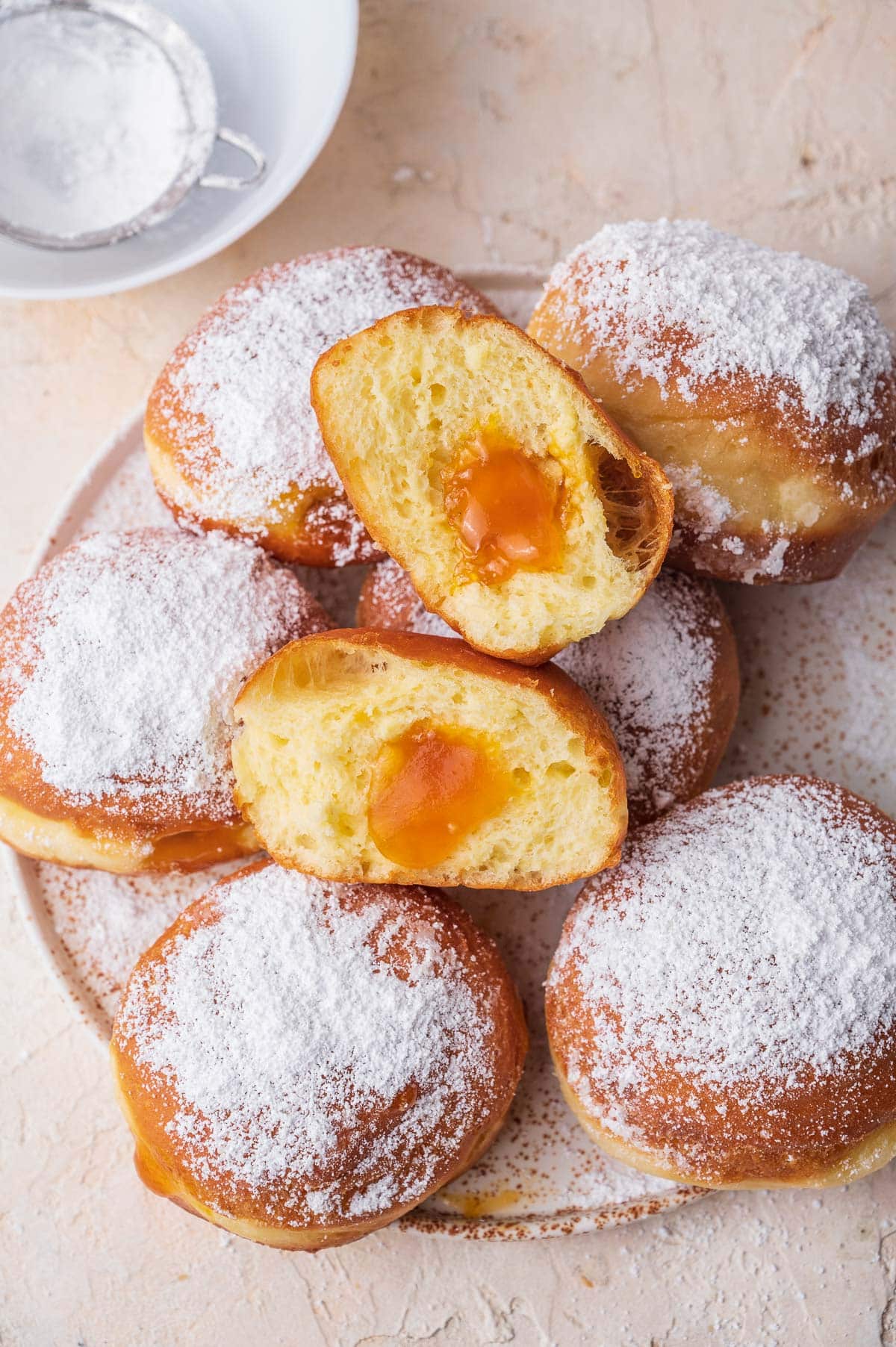 Krapfen dusted with powdered sugar on a white plate. One Krapfen is cut in half.