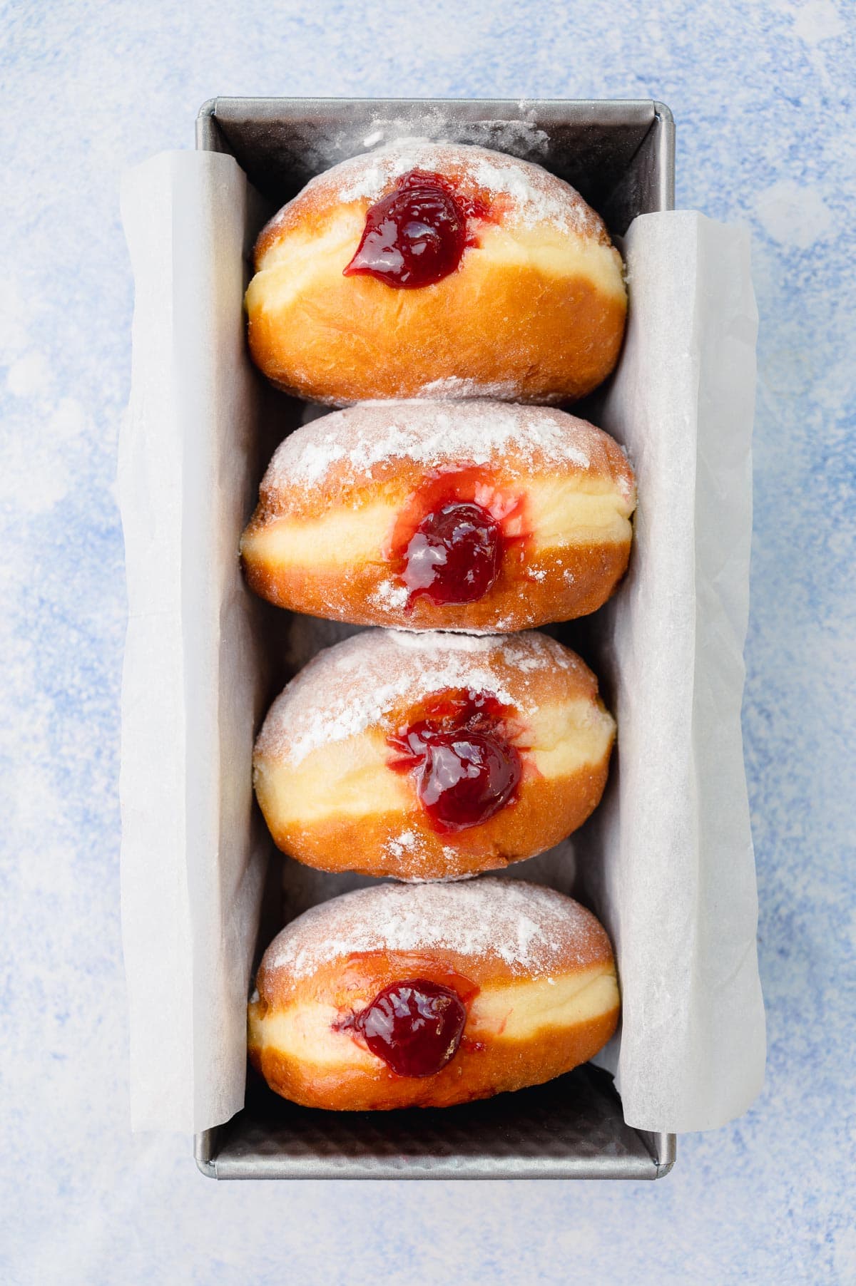 Overhead photo of paczki in a loaf pan on a blue background.