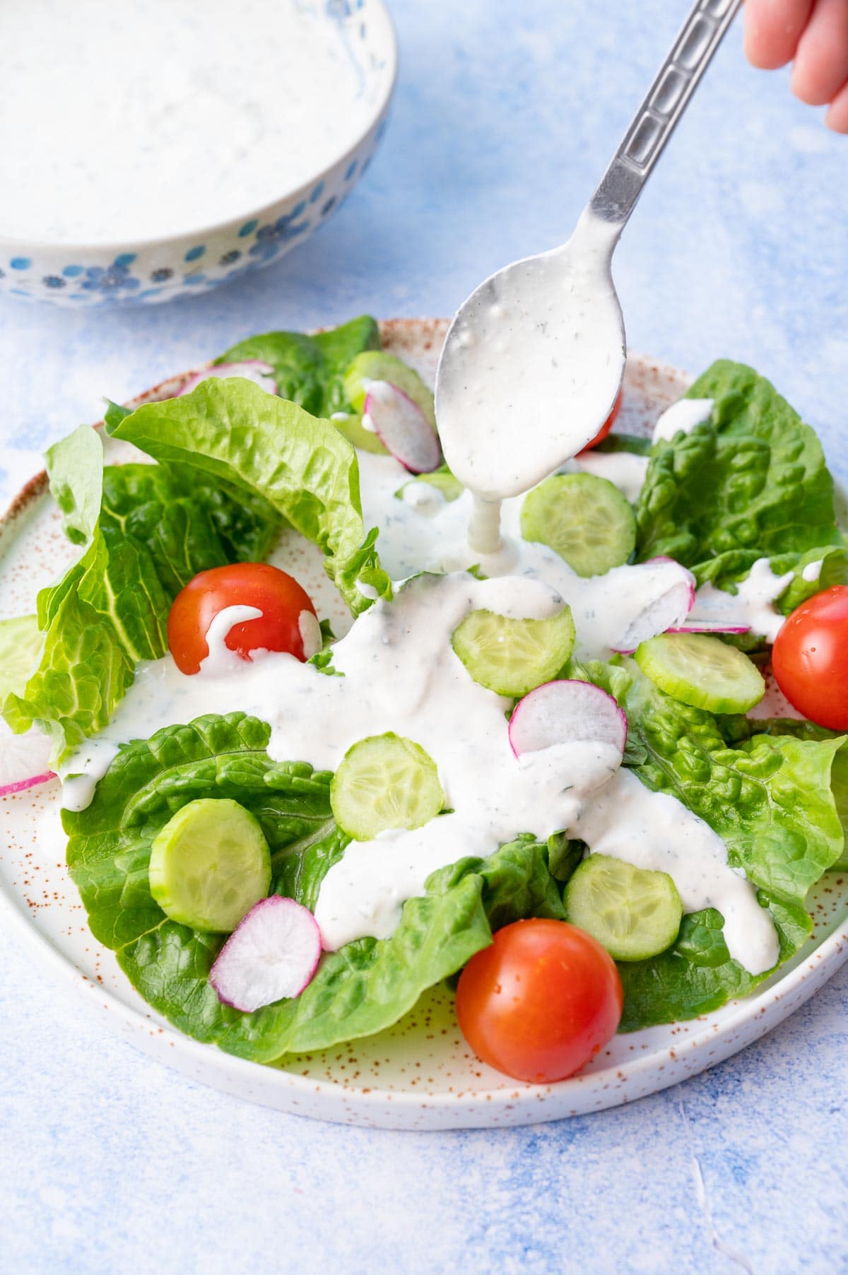 Ranch dressing is being spooned over a salad on a white plate.