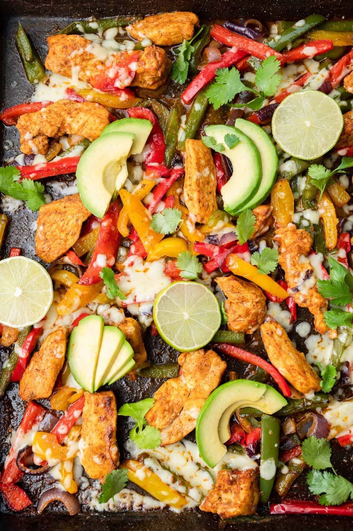 Sheet pan chicken fajitas on a black baking sheet.