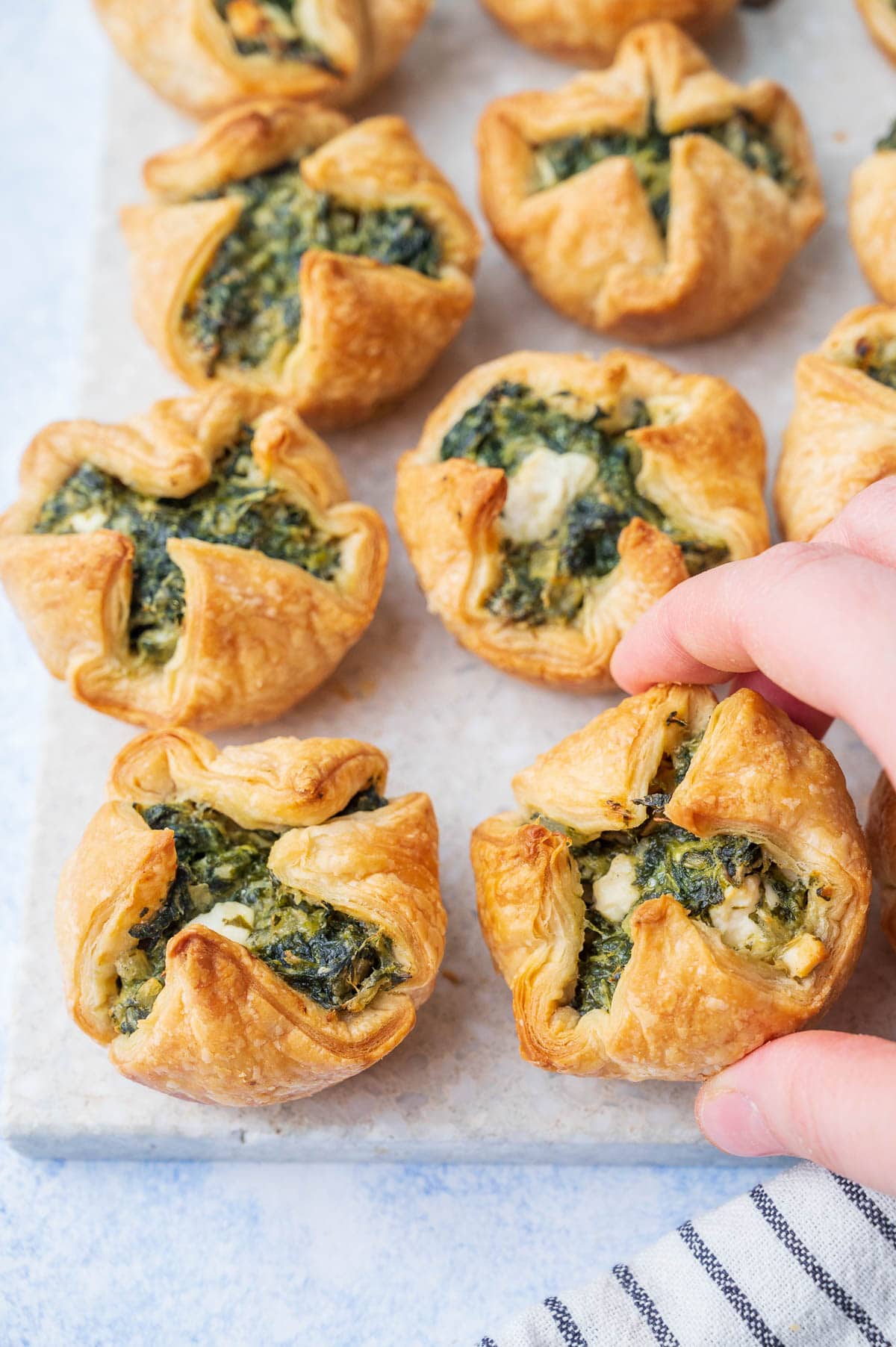 Spinach puffs on a grey stone board. One spinach puff is held in a hand.