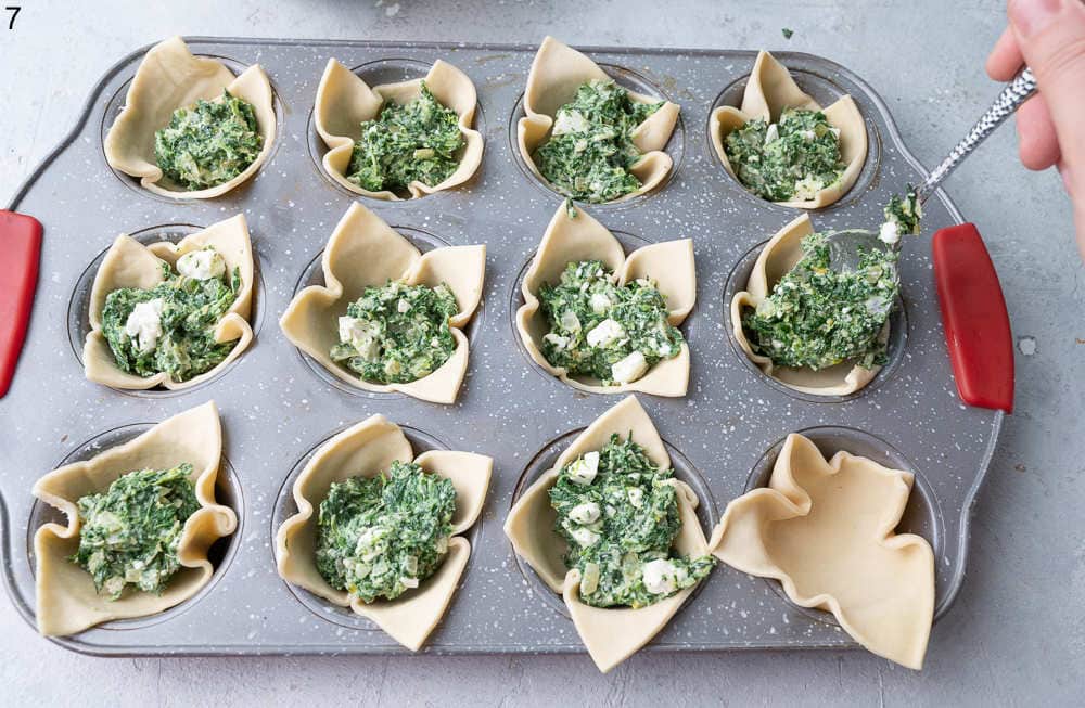 Spinach cheese filling is being put into puff pastry cups.