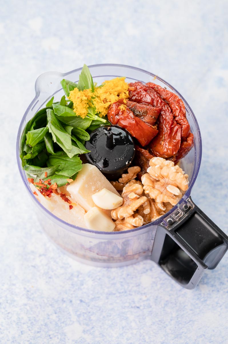 Ingredients for sun-dried tomato pesto in a food processor bowl.