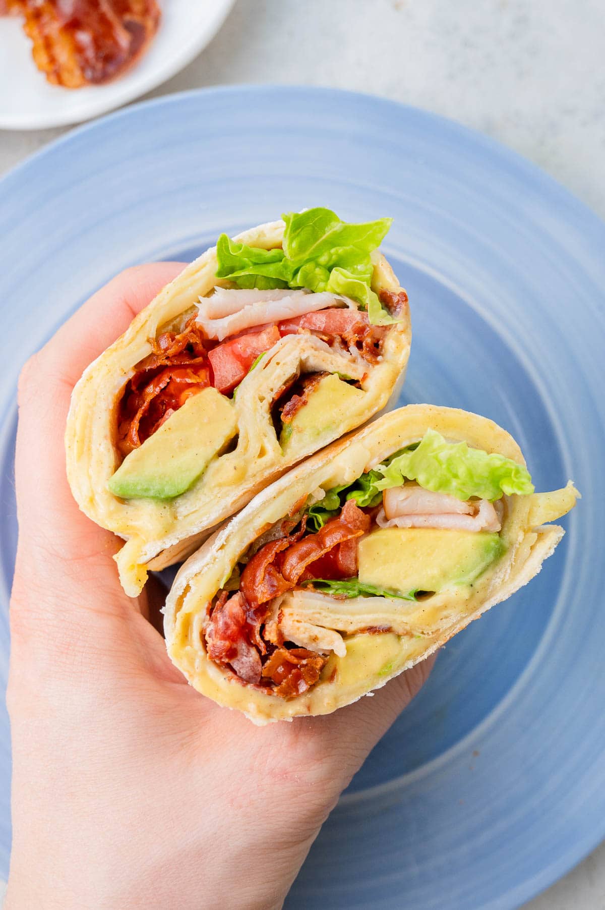 Two halves of a turkey wrap are being held in a hand. A blue plate in the background.