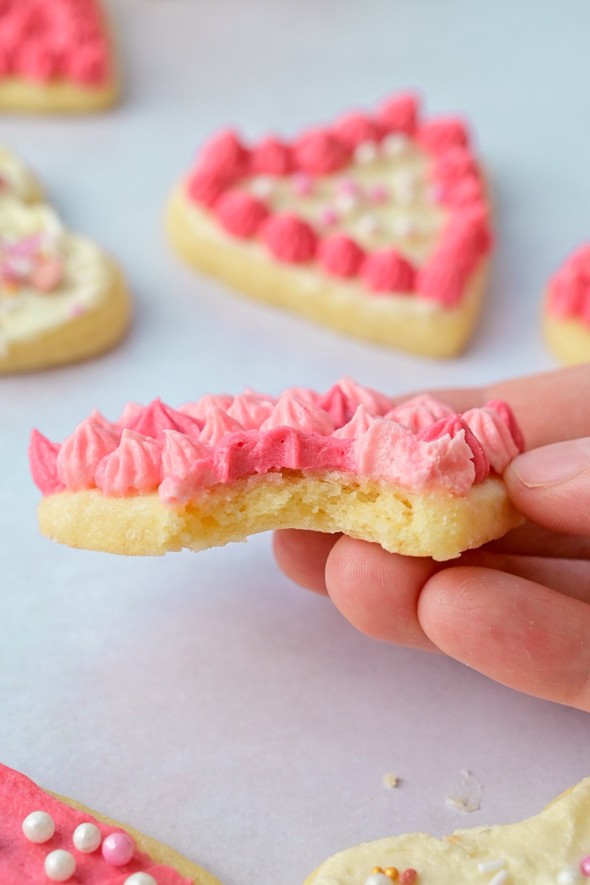Heart cookie with frosting and a piece missing is being held in a hand.
