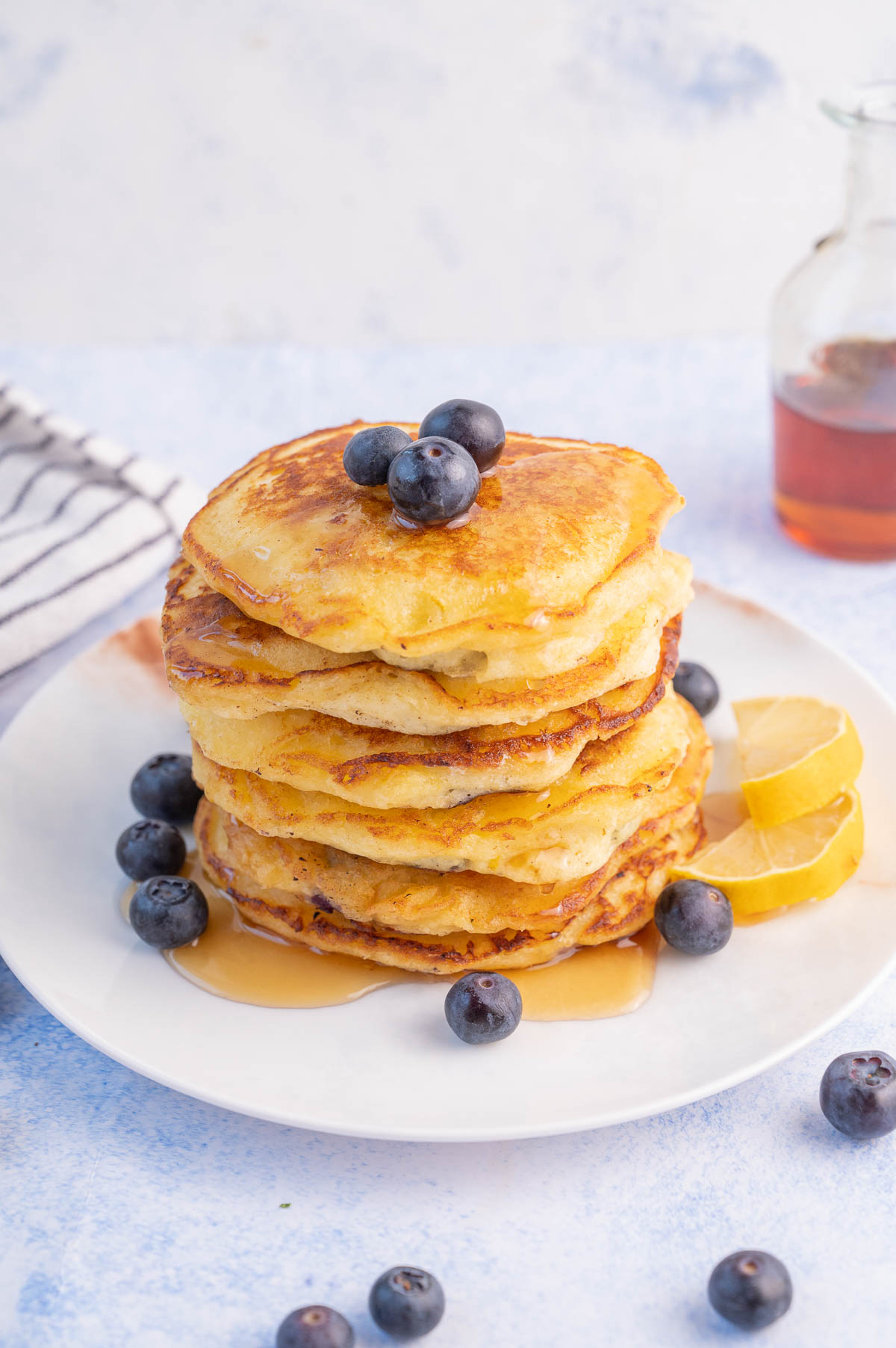 A stack of blueberry buttermilk pancakes on a white plate with blueberries and lemon slices.